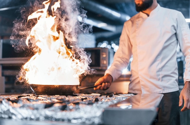 Frigideira está pegando fogo Chef de uniforme branco cozinhando comida na cozinha Dia ocupado no trabalho