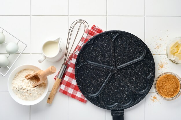 Frigideira vazia preta, frigideira com revestimento antiaderente de pedra para assar panquecas em forma de corações de café da manhã e ingredientes no fundo da mesa de concreto cinza. Café da manhã para o dia dos namorados. Vista do topo.