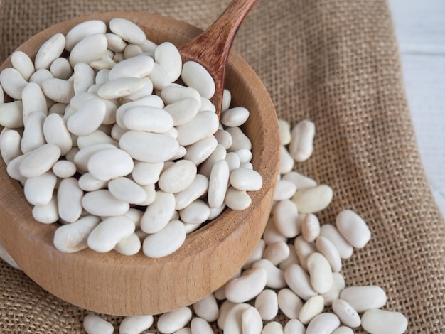 Frijoles blancos en una cuchara de madera sobre una mesa de madera blanca, espacio de copia