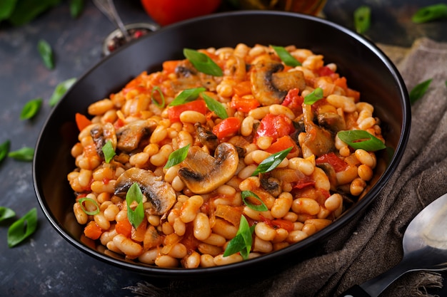 Frijoles blancos guisados con champiñones y tomates con salsa picante en un recipiente negro.