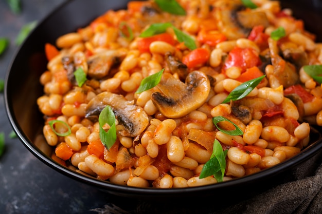 Frijoles blancos guisados con champiñones y tomates con salsa picante en un recipiente negro.