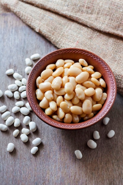 Frijoles blancos hervidos en un recipiente rústico con frijoles crudos sobre la mesa