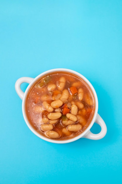 Frijoles blancos hervidos con verduras y salsa en un tazón blanco