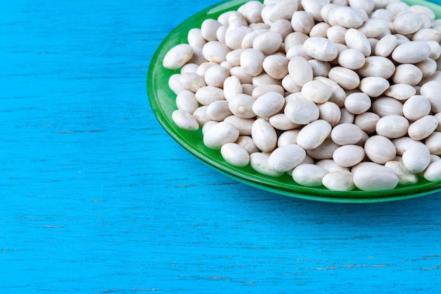 Frijoles blancos en un plato verde sobre un fondo de madera azul