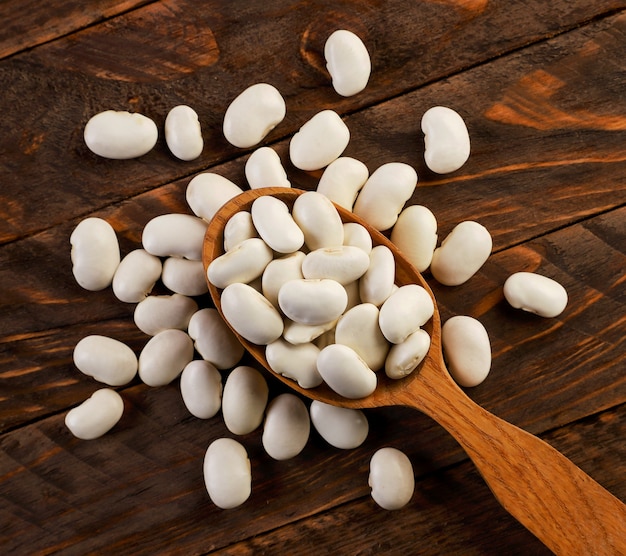 Frijoles blancos en primer plano de una cuchara sobre un fondo de madera. La vista desde arriba