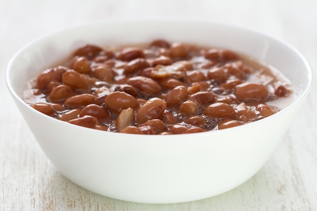 Foto frijoles cocidos en plato blanco sobre mesa de madera blanca