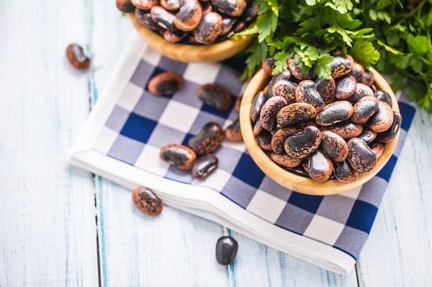 Frijoles crudos en cuencos de madera con hierbas de perejil en la mesa de la cocina.