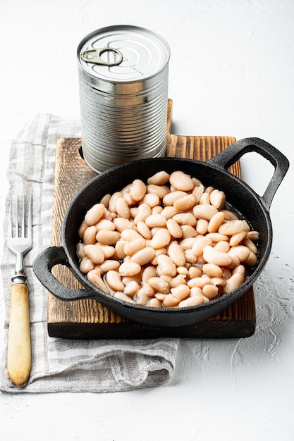 Frijoles enlatados blancos, con lata de metal, en una sartén de hierro fundido, sobre la superficie de piedra blanca