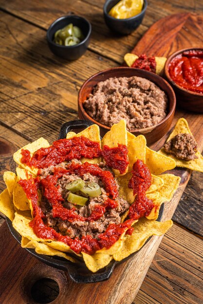 Frijoles refritos mexicanos tradicionales con nachos jalapeños y salsa de tomate Fondo de madera Vista superior