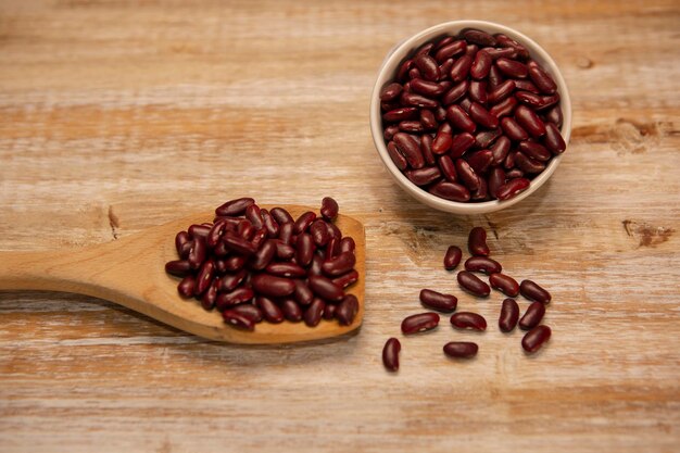 Frijoles rojos en una cuchara y en un recipiente sobre fondo de madera