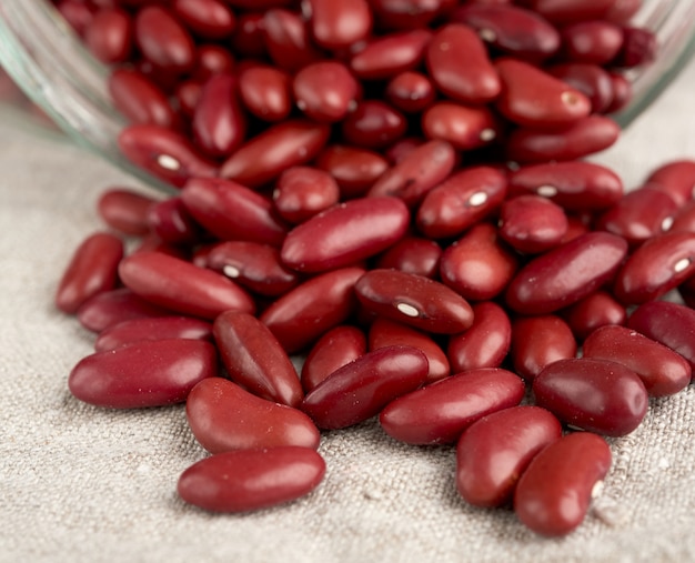 Foto frijoles rojos dispersos de un frasco de vidrio sobre una servilleta de lino gris