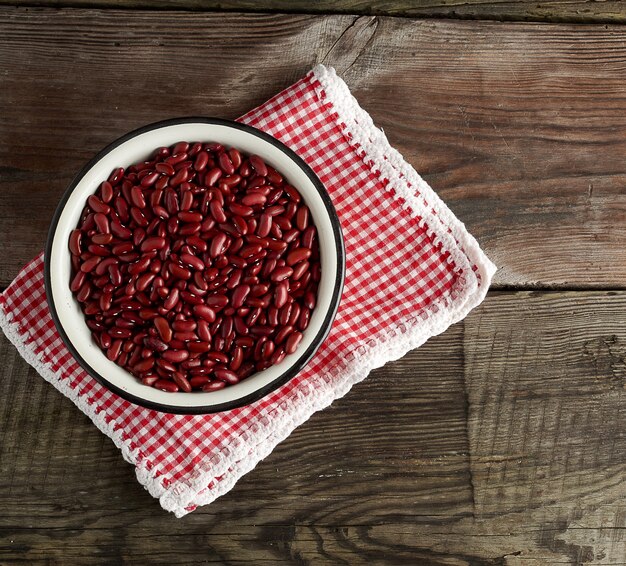 Foto frijoles rojos ovales crudos en un plato sobre una mesa de madera