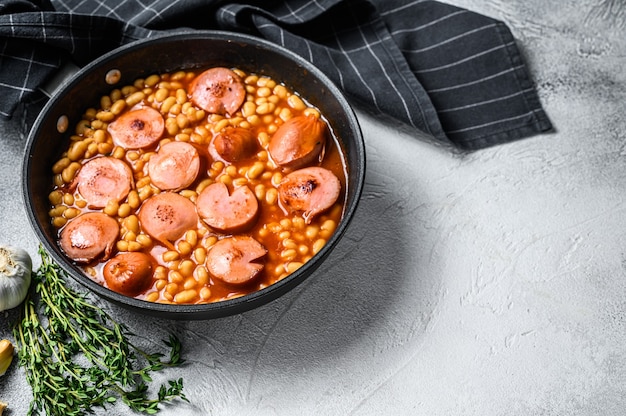 Frijoles con salchichas en salsa de tomate en una sartén. Fondo blanco. Vista superior. Copie el espacio.