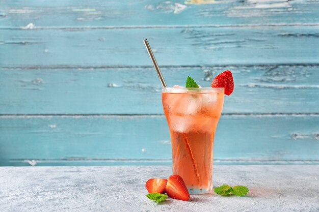 Frío y refrescante bebida de fresa de verano en vidrio contra la pared azul claro.