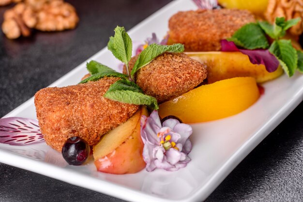 Frisch duftende Käsesticks mit Bratapfel und Pfirsich verziert mit Blumen auf einem weißen Teller