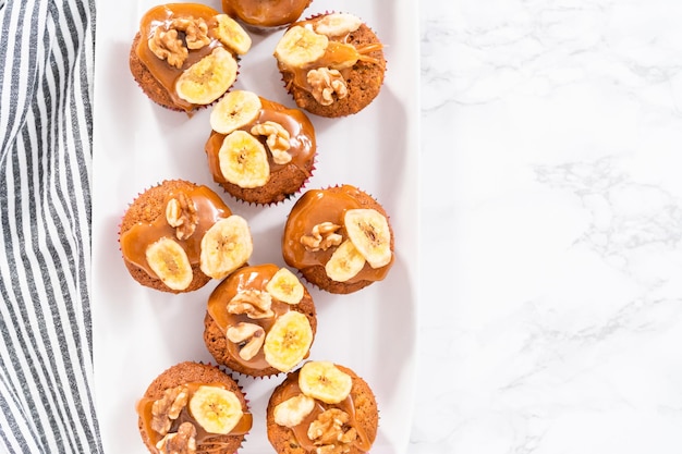 Frisch gebackene Bananen-Nuss-Brot-Muffins, beträufelt mit hausgemachtem Karamell, dekoriert mit Walnüssen und Bananenchips.