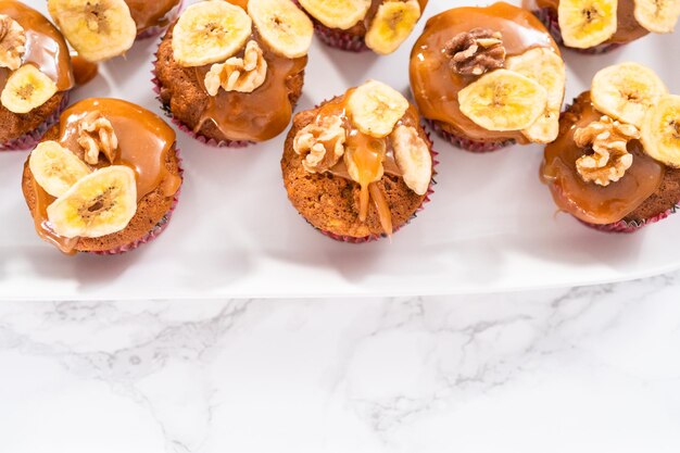 Frisch gebackene Bananen-Nuss-Brot-Muffins, beträufelt mit hausgemachtem Karamell, dekoriert mit Walnüssen und Bananenchips.