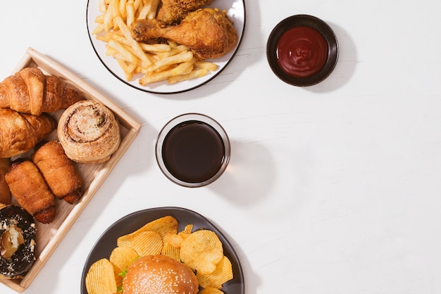 Frisch gebackene Brötchen, großer Hamburger, gebratenes knuspriges Hühnchen und Pommes Frites auf weißem Tisch - ungesundes Lebensmittelkonzept