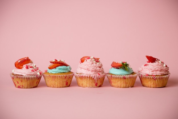 Frisch gebackene bunte Cupcakes verziert mit Streuseln und Erdbeeren auf rosa Hintergrund