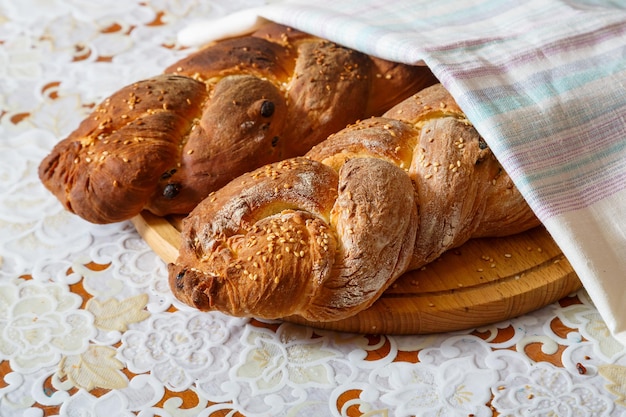 Frisch gebackene Challah mit Sesam für Schabbat auf einem Holzbrett auf einer weißen Tischdecke