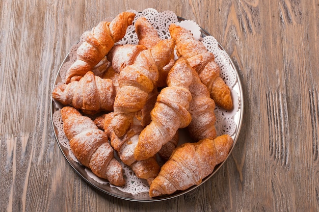 Frisch gebackene Croissants auf einer runden Platte, Draufsicht. Croissants auf einem Holztisch