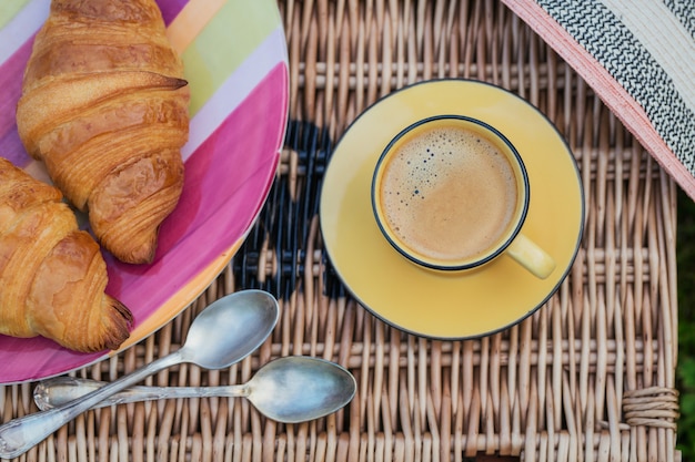 Frisch gebackene Croissants mit Kaffee. Zwei französische Croissants und eine Tasse Kaffee auf Weidenkorb. Ansicht von oben