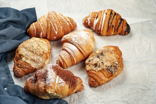 Frisch gebackene Croissants mit verschiedenen Füllungen auf Pergament. Appetitliches französisches Gebäck zum Frühstück. Unterschiedliches Sortiment, viele Croissants