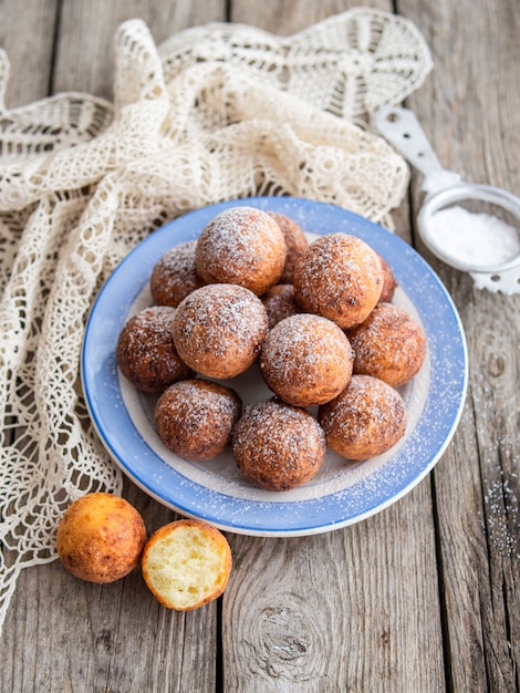 Foto frisch gebackene käsedonuts mit puderzucker auf dem teller auf rustikalem holztisch. die atmosphäre eines gemütlichen frühstücks zu hause. nahaufnahme, speicherplatz kopieren.