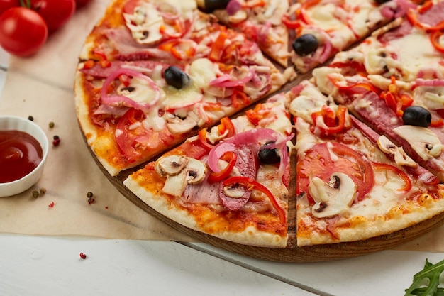 Frisch gebackene Pizza mit geräucherten Würstchen, Paprika, Pilzen, Zwiebeln und Oliven, serviert auf Holzhintergrund mit Tomatensoße und Kräutern Food-Delivery-Konzept Restaurantmenü