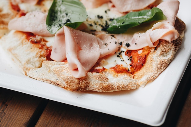 Frisch gebackene Pizza mit geschmolzenem Käse italienische Kräuter und Tomatensoße und frischem Basilikum auf einer weißen Platte auf einem selektiven Fokus der Küche