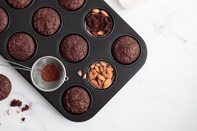 Frisch gebackene Schokoladenmuffins in einer Backform auf weißem Tisch mit Zutaten