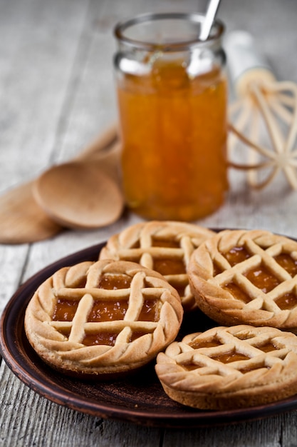 Frisch gebackene Törtchen mit Marmeladen- oder Aprikosenmarmeladenfüllung und auf Keramikplatte und Küchenbäckereigerät.