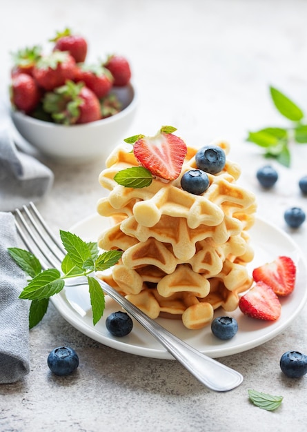 Frisch gebackene Waffeln mit Erdbeeren und Blaubeeren auf einem grauen Hintergrund aus Beton