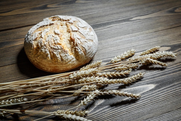 Frisch gebackener Brotlaib und Weizenähren, die auf einem hölzernen Hintergrund liegen