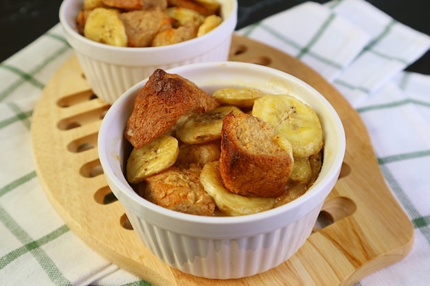 Frisch gebackener hausgemachter Bananenbrotpudding in der Keramikschale auf hölzernem Brotbrett