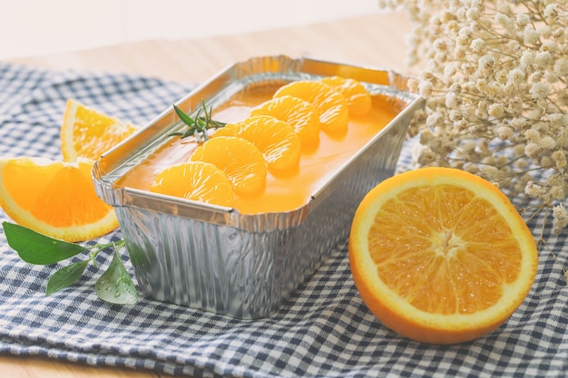 Foto frisch gebackener mandarinen-orangen-biskuitkuchen, dekoriert mit orangengeleesauce und orangenpulpe in aluminiumfolienbrot.