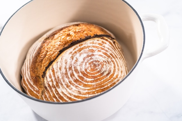 Frisch gebackenes Brot aus Weizensauerteig mit Markierungen aus dem Brotkorb im holländischen Ofen aus emailliertem Gusseisen.