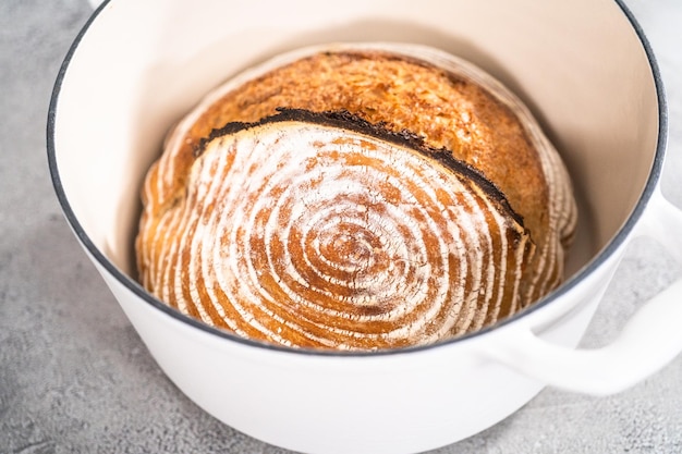 Frisch gebackenes Brot aus Weizensauerteig mit Markierungen aus dem Brotkorb im holländischen Ofen aus emailliertem Gusseisen