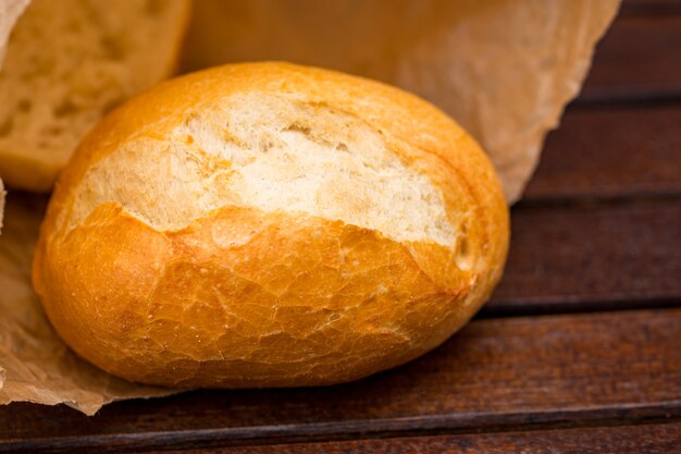 Frisch gebackenes Brot in Papier eingewickelt, auf Holzuntergrund.