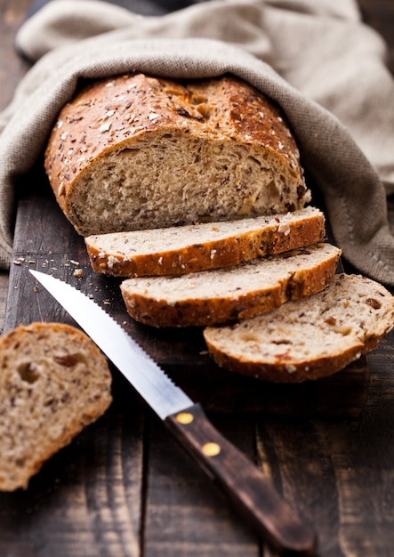 Foto frisch gebackenes brot mit geschirrtuch und messer auf dunklem hölzernem brett