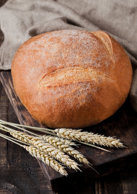 Frisch gebackenes Brot mit Geschirrtuch und Weizen auf dunklem hölzernem Brett