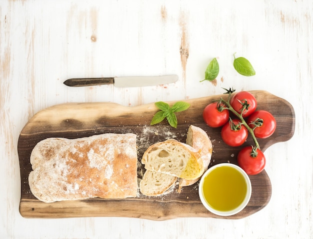 Frisch gebackenes Ciabatta-Brot mit Kirschtomaten, Olivenöl, Basilikum und Salz auf Walnussholzbrett über weißer, Draufsicht