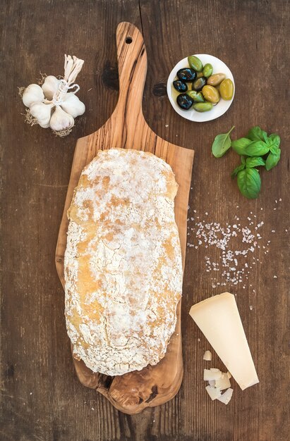 Frisch gebackenes Ciabatta-Brot mit Knoblauch, mediterranen Oliven, Basilikum und Parmesan auf Servierbrett