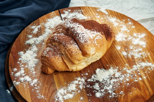 Frisch gebackenes Croissant mit Kondensmilch und Schokoladenüberzug auf einem Holzbrett. Appetitliches französisches Gebäck zum Frühstück