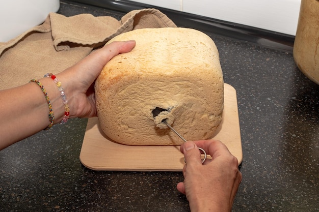 frisch gebackenes hausgemachtes Brot aus einer Brotmaschine Die Hausfrau nimmt ein Messer aus dem Brot, um den Teig zu kneten