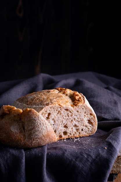 Frisch gebackenes hausgemachtes Sauerteigbrot auf dunkler Leinenserviette, Holztisch.