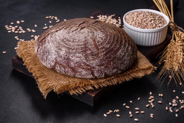 Frisch gebackenes hausgemachtes Schwarzbrot auf schwarzem Betongrund mit Weizenkörnern