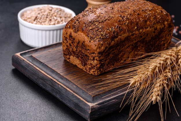 Frisch gebackenes Schwarzbrot mit Ähren und Weizenkörnern auf dunklem Betonhintergrund