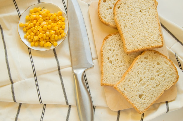 Frisch gebackenes traditionelles Weizenbrot, Maiskörner und Messer auf Leinengeschirrtuch, flache Lage