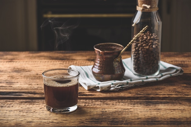 Frisch gebrühter türkischer Kaffee im Trinkglas. Cezve und Glas geröstete Kaffeebohnen.